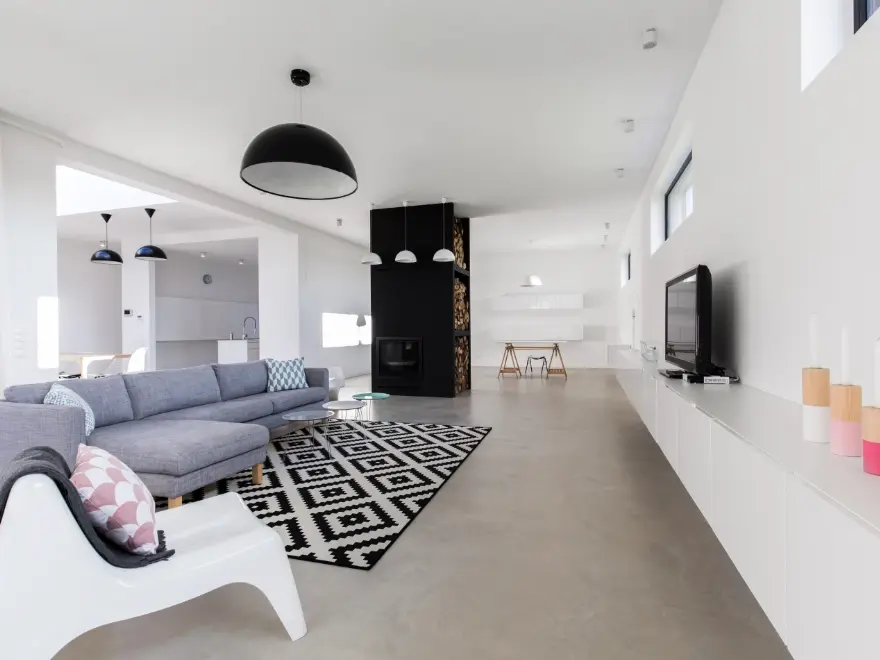 Salón moderno con suelo de microcemento gris, paredes blancas y chimenea negra en vivienda de Elche
