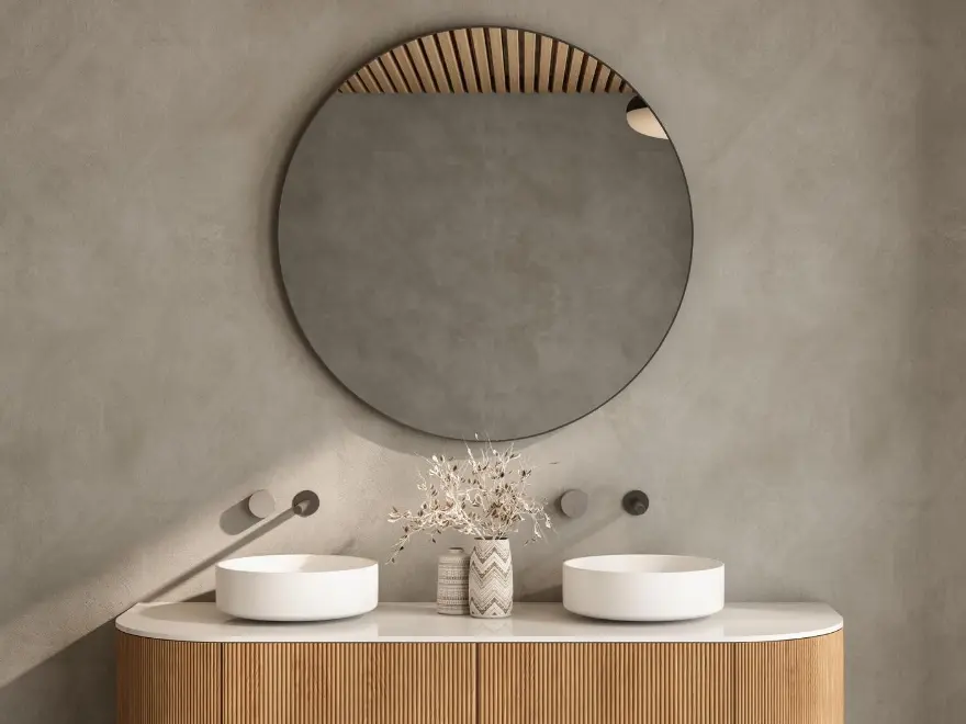 Detalle de baño con pared de microcemento gris, doble lavabo sobre mueble de madera y espejo redondo en Elche