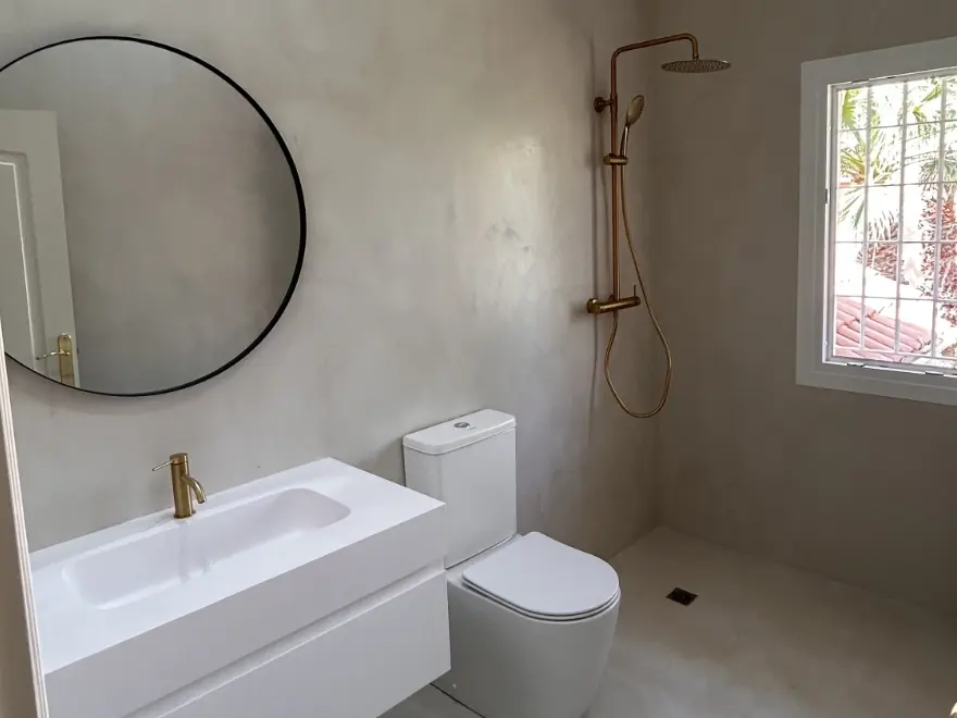 Baño completo con microcemento gris, bañera integrada, WC y ducha con grifería dorada en Elche