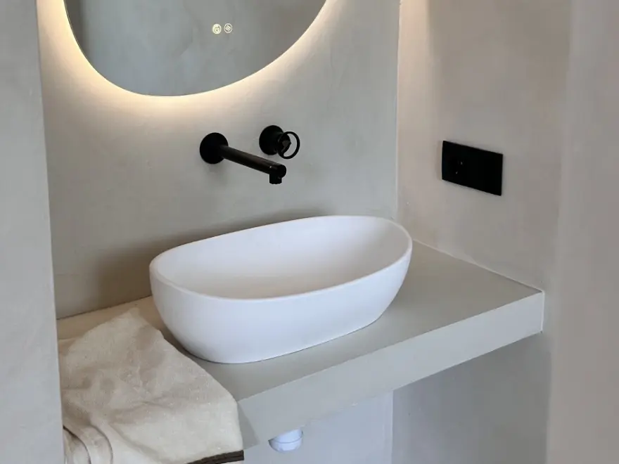 Detalle de baño con microcemento gris, lavabo redondo sobre encimera y espejo redondo con luz LED en Elche