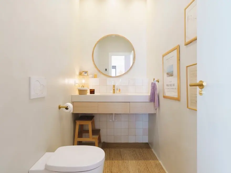 Baño con microcemento blanco, lavabo suspendido, WC y espejo redondo en vivienda de Elche