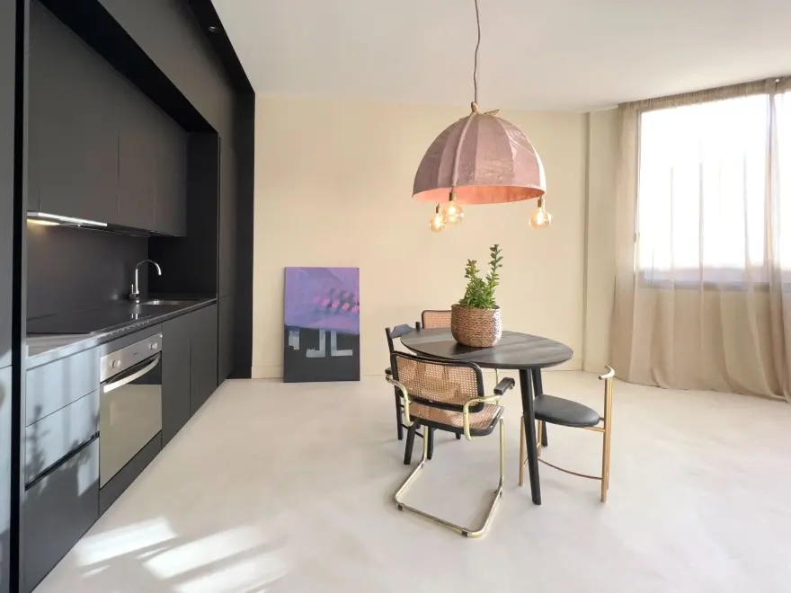 Cocina comedor con suelo de microcemento beige, muebles negros y lámpara colgante de cobre en Elche