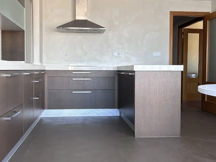Cocina con suelo de microcemento gris, muebles grises y campana extractora en vivienda de Elche