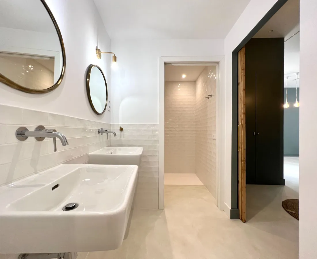 Baño con suelo de microcemento beige claro, doble lavabo blanco y ducha con azulejo metro en Elche