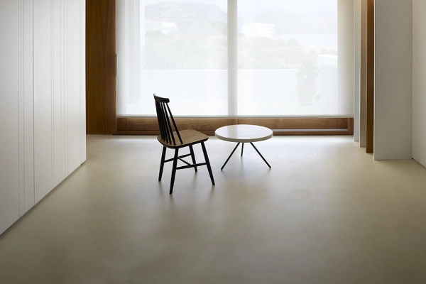 Suelo de microcemento beige claro en espacio minimalista con silla negra y mesa redonda en Elche