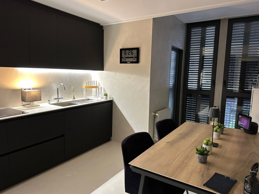 Cocina con suelo y pared de microcemento gris claro, muebles negros y mesa de madera en Elche