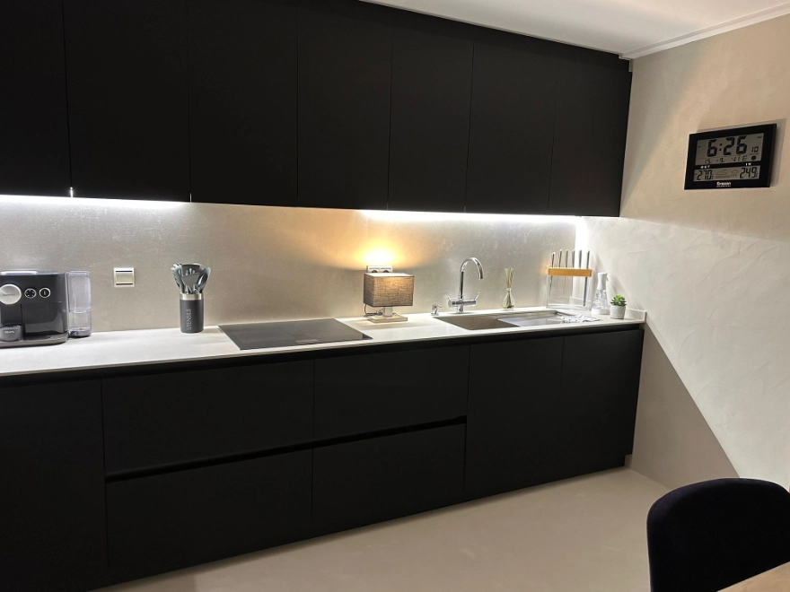 Detalle de cocina con microcemento en pared y suelo, muebles negros mate e iluminación LED en Elche