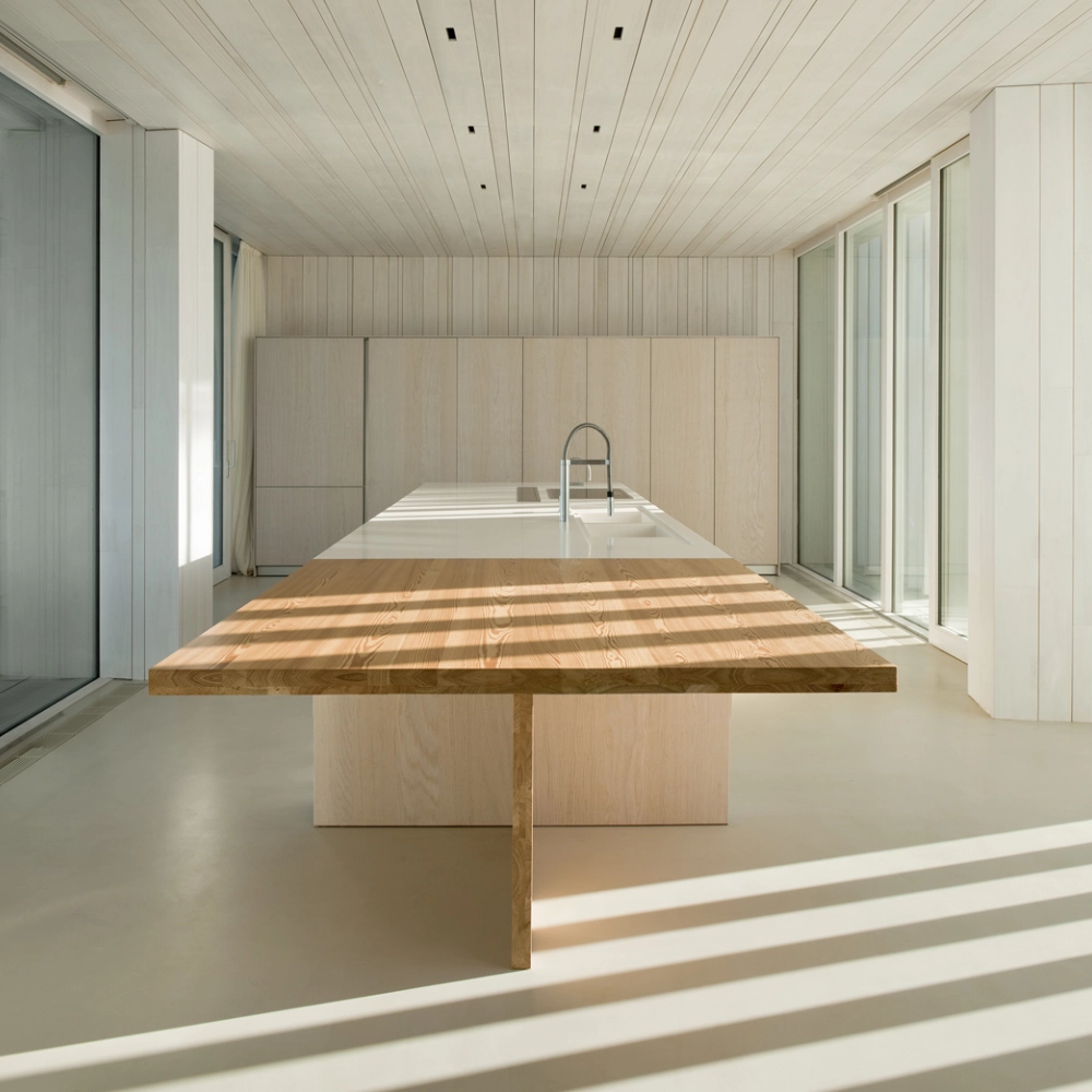 Suelo de microcemento gris claro en cocina minimalista con isla y mesa de madera natural en Elche