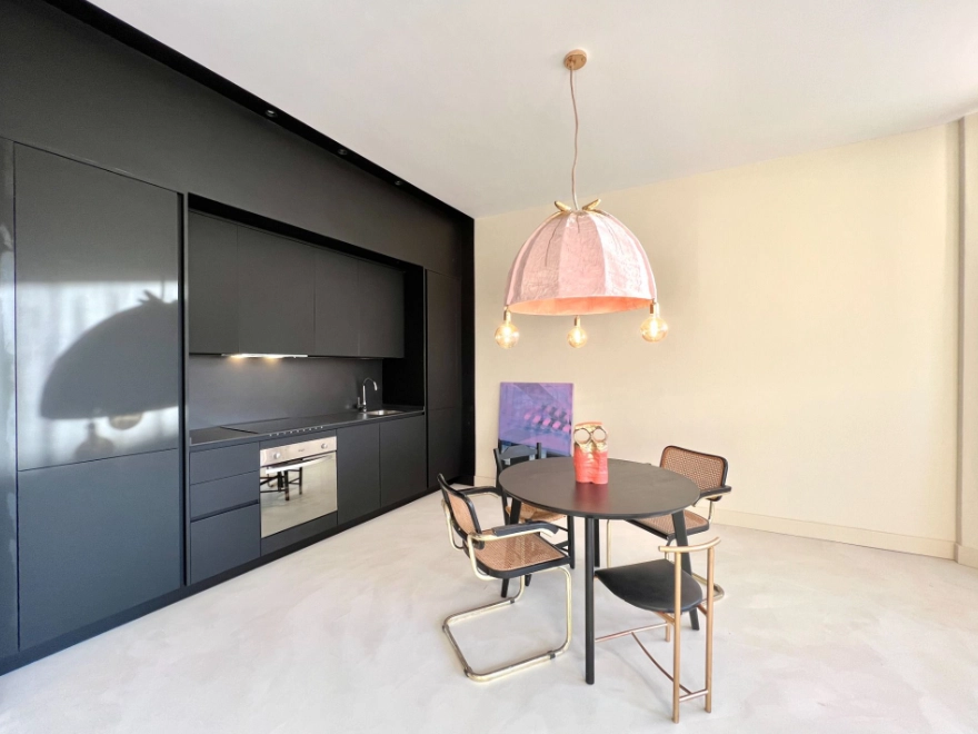 Suelo de microcemento gris claro en cocina comedor con muebles negros y lámpara rosa en Elche