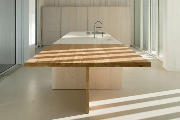 Suelo de microcemento gris claro en cocina minimalista con mesa de madera maciza e isla blanca en Elche
