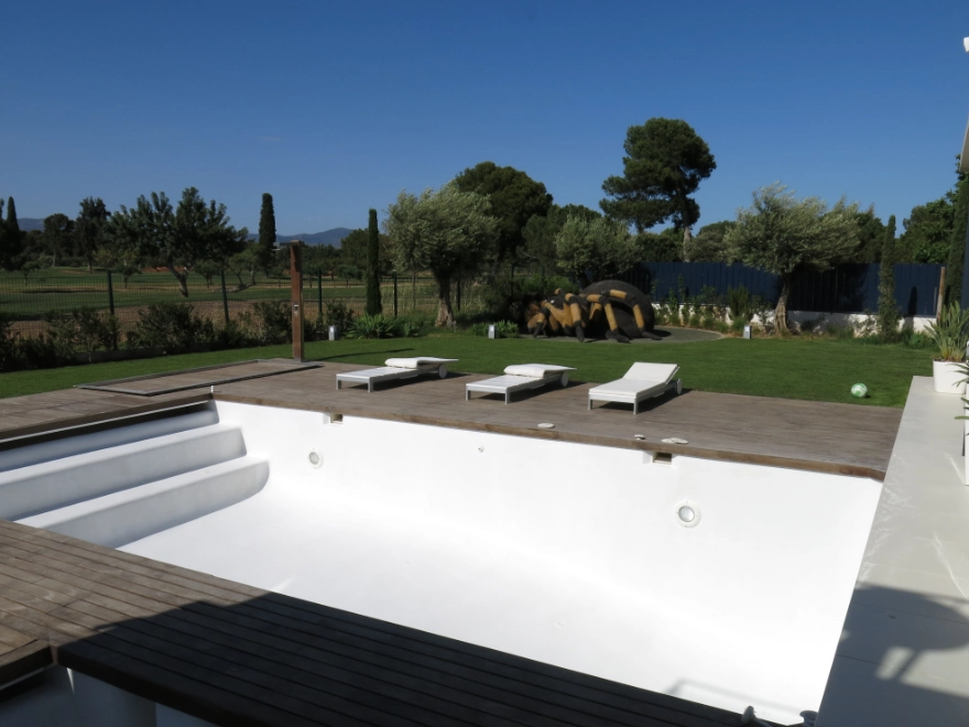 Piscina con microcemento blanco y terraza de madera con tumbonas en jardín de chalet en Elche