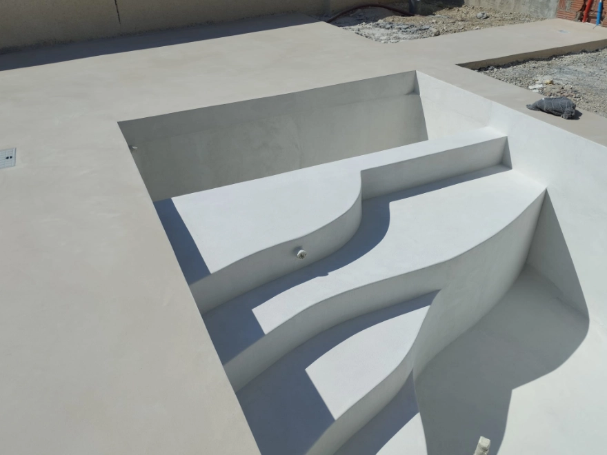 Detalle de escalera de piscina con microcemento blanco y muro de piedra natural en Elche