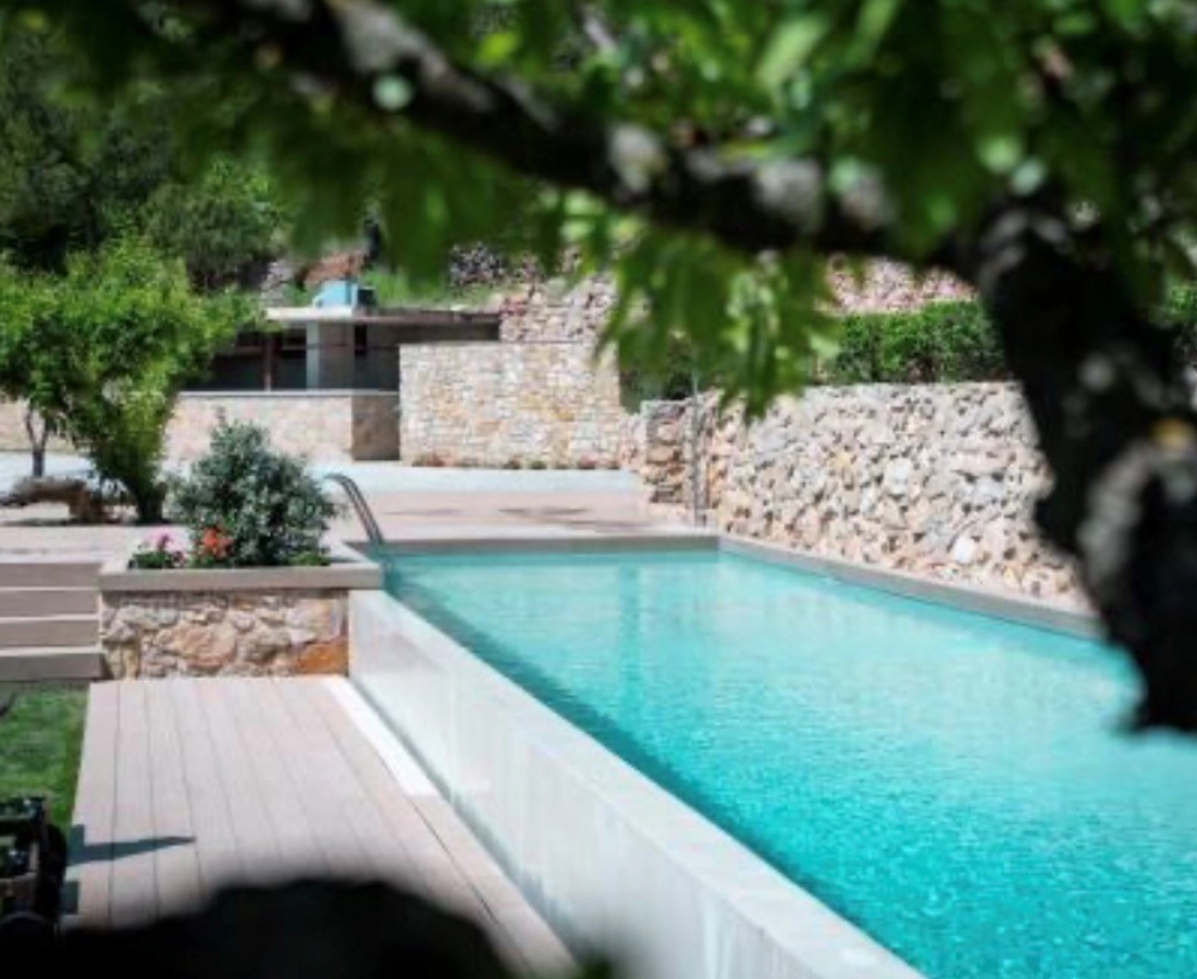 Piscina con microcemento turquesa y bordes de piedra natural en jardín de chalet en Elche
